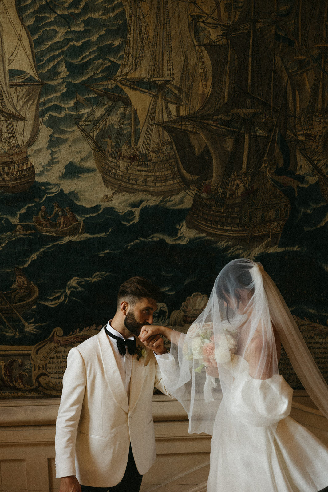 Groom kissing the bride's hand as they walk down the grand staircase in a french countryside chateau
